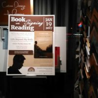 Book signing and reading poster in window of art gallery and frame shop